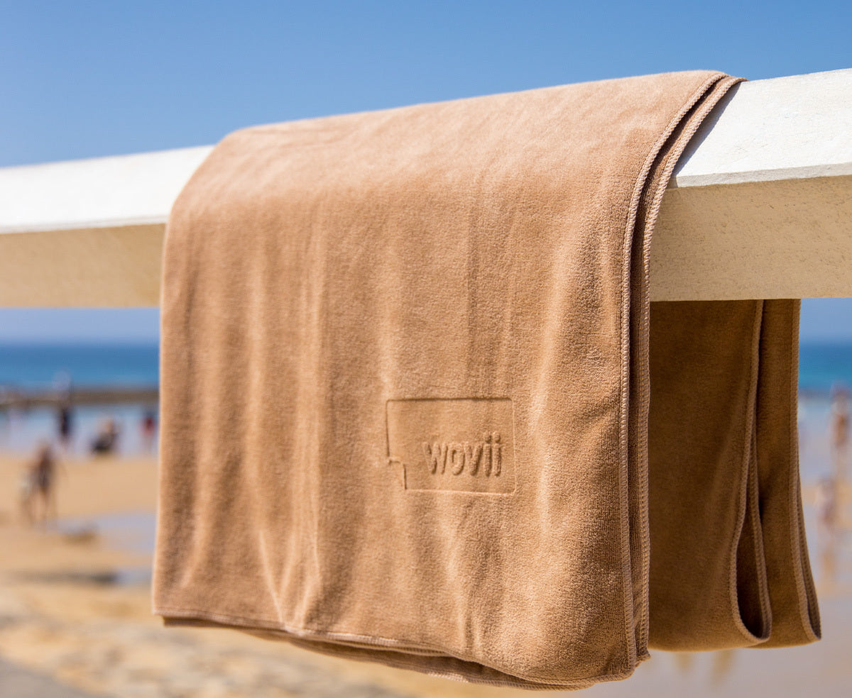 Wovii coffee coloured beach towel hanging on a wood railing